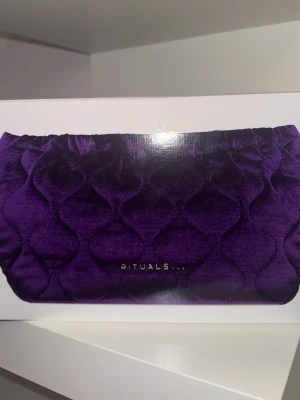 Lila sammet clutch från Rituals - En lila oöppnad, helt ny clutch i mjuk sammet från Rituals med quiltat mönster och guldfärgad logga framtill. Perfekt att ha hemma eller ge bort som gåva. Den innehåller även duschskum 200 ml, kroppskräm 150 ml, rumsdoft 200 ml, minidoftstickor 70 ml, handbalm 70 ml 