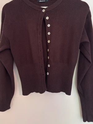 Brun ribbad kofta med vita knappar från Gina Tricot  - Mysig brun kofta med ribbad midja och långa ärmar från Gina Tricot i storlek S