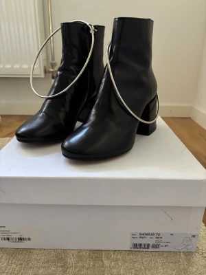 Maison margiela ankle boots - Unika svarta stövletter i skinn med höga, chunky klackar och stora silverringar som cool detalj. Stövletterna har en stilren siluett och dragkedja på insidan för enkel påtagning. Perfekt för dig som gillar statement-accessoarer och modern design. Nypris ungefär 7000kr vid minsta fundering eller intresse är det bara att höra av sig 👍🏼