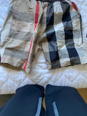 Rutig shorts med breda ränder - Snygga shorts med stora rutiga mönster i beige, svart, grått och röda detaljer. De har elastisk midja och är perfekta för en avslappnad stil. Materialet känns lätt och passar bra till varmare dagar.