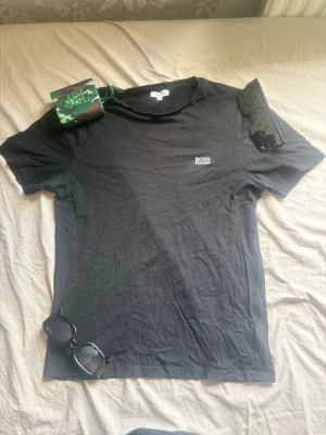 Svart t-shirt från Hugo Boss - Svart t-shirt från Hugo Boss med klassisk passform och diskret logga på bröstet. Tillverkad i mjuk bomull som känns skön mot huden. Perfekt till jeans eller shorts för en clean och enkel stil.Pris kan diskuteras.