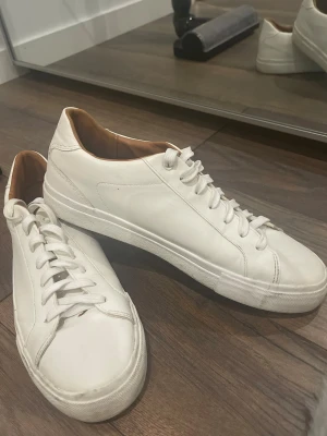 Vita sneakers i skinn från ZARA - Stilrena vita sneakers från ZARA i skinn med klassisk låg profil och vita snören. Insidan är ljusbrun och sulan är vit. Perfekta för en clean och enkel look.