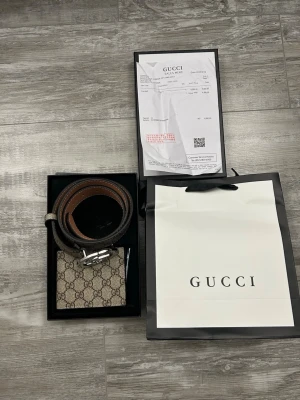 Gucci GG Supreme bälte med silverdetalj - Säljer ett klassiskt Gucci GG Supreme bälte i beige och brunt med det ikoniska GG-mönstret och en stor rund silverfärgad spänne. Bältet är gjort i canvas med skinn på insidan och passar perfekt till att lyfta vilken outfit som helst.