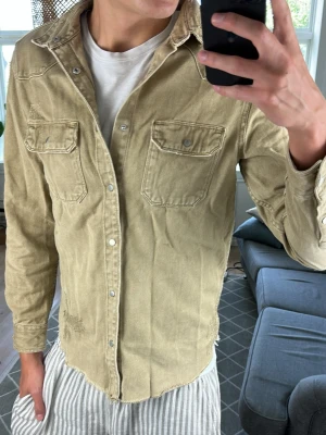 Jeansskjorta/Overshirt Olivgrön/Beige - Väldigt snygg och super trendig overshirt med många snygga och tilltänkta slitningar.  Skriv vid fundering!😇🙌 Mått: A:47 B:42 C:45 D:66 