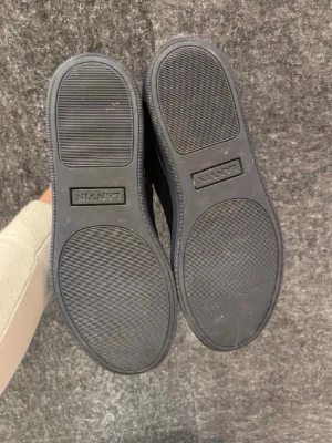Svarta sneakers från Lanvin - Snygga svarta sneakers från Lanvin med ovandel i mocka och lackad tå. Skorna har svarta snören, metallfärgade öljetter och en svart gummisula. Perfekta för dig som gillar stilrena och exklusiva detaljer. Finns ingen påse och box så ni vet tappa bort. Kan gå ner vi snabb affär 
