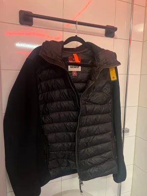 Svart warm-up från Parajumpers - Säljer en svart pufferjacka från Parajumpers med klassisk gul detalj vid kragen och dragkedja framtill. Jackan har quiltad design, hög krage och sidofickor med dragkedja. Perfekt för kalla vinterdagar och riktigt snygg streetstil. Köpt på Kauffman i köpenhamn