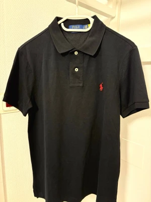 Svart pikétröja från Polo Ralph Lauren - Klassisk svart pikétröja från Polo Ralph Lauren. Size L men sitter som en Custom Slim M. Aldrig använd bara provad! 