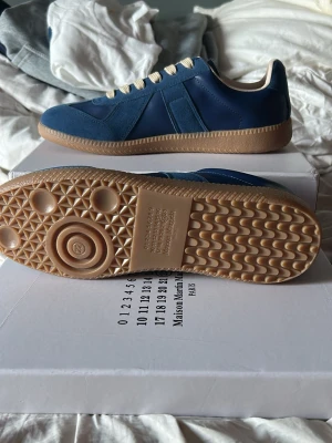 Blå sneakers med beige sula - Snygga blå sneakers med beige detaljer och klassisk gummisula. Skorna har vita snören och ovandel i både mocka och slätt material för en stilren look. Perfekta för dig som gillar minimalistisk design och vill ha något som sticker ut utan att vara för mycket.
