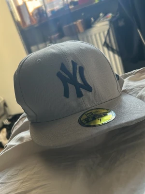 Beige New York Yankees keps - Helt ny Snygg beige New York Yankees keps från New Era med mörkblått broderat NY-logga framtill och texten 'New York or Nowhere' på sidan. Klassisk 59FIFTY-modell med rak skärm och broderade ventilationshål. Perfekt för dig som gillar streetwear och sportig stil.