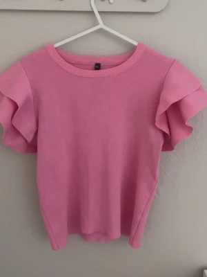 Rosa topp med volangärmar - Supersöt rosa topp från Golden Days med volangdetaljer på ärmarna. Toppen har rund halsringning och är tillverkad i ett mjukt material som känns bekvämt mot huden. Perfekt för dig som vill ha en feminin och trendig look.🎀