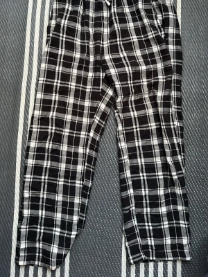 pyjamasbyxor i svartvitt - Säljer ett par pyjamasbyxor med svartvitt rutmönster. Byxorna har resår i midjan med dragsko och är tillverkade i ett mjukt, lätt tyg som passar perfekt för att chilla hemma. Klassisk och avslappnad passform.