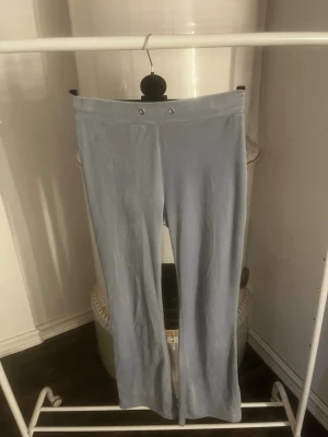 Ljusblå mjukis från Gina - Säljer ett par ljusblå mjukis med utsvängda ben och hög midja. De har två dekorativa knappar framtill och två bakfickor. Materialet ser ut att vara mjukt och stretchigt, perfekt för en avslappnad look.