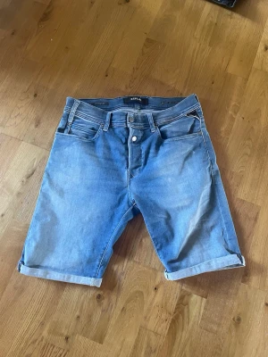 Ljusblå jeansshorts från Replay - Säljer ett par ljusblå jeansshorts från Replay, modell RBJ 901 SHORT. Klassisk femficksdesign, uppvikta benslut och knappgylf. Perfekta för sommaren och riktigt sköna att bära till t-shirt eller hoodie.