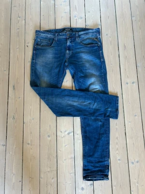 Blå slim fit jeans från Replay - Snygga blå slim fit jeans från Replay med klassisk femficksdesign och slitningar på låren och knäna. Jeansen har normal midja, dragkedjegylf och är tillverkade i ett mjukt denimtyg som ger en skön passform.