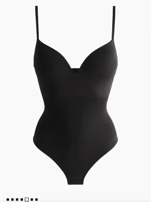 Trendig urringad body - Snygg och populär svart bodysuit med tunna, justerbara axelband och v-ringad urringning. Bodyn är aldrig använd och är i nyskick.