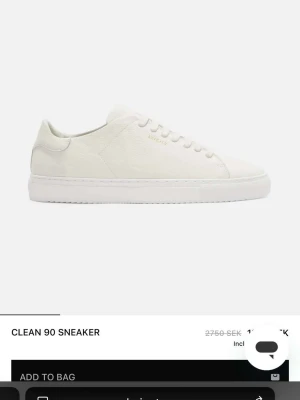Axel Arigato - Säljer ett par vita Clean 90 sneakers från Axel Arigato. Skorna har en stilren och minimalistisk design med ovandel i slätt läder, vita snören och diskret logga i guld på sidan. Klassisk låg modell med vit sula som passar till allt. Påse och låda medföljer helt nya skor 