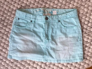 Ljusblå kort jeanskjol - Säljer en ljusblå kort jeanskjol med fem fickor och knappstängning fram. Kjolen har klassisk denimlook med bälteshällor och raka sömmar. Jätte snygg till sommaren och har en väldigt trendig look!💕XS till S 