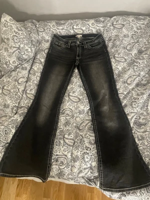 Svarta bootcut jeans med slitningar - Snygga svarta bootcut jeans med ljusa slitningar framtill och bakfickor med dekorativa sömmar. Jeansen har låg midja och är perfekta för dig som gillar lite coolare jeans!