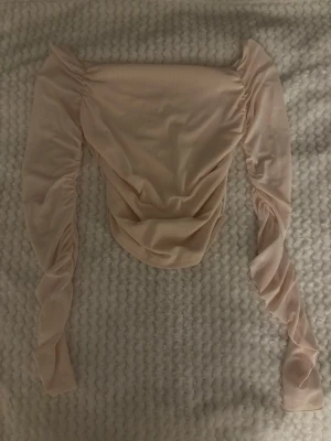 Beige mesh topp från Cider - Trendig beige mesh topp från Cider med långa, rynkade ärmar och croppad passform. Toppen har en snygg drapering framtill och är tillverkad i ett tunt, stretchigt material som känns lätt och luftigt.