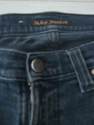 Svarta nudie jeans slim/skinny - Snygga mörkblå bootcut jeans med klassisk femficksdesign och lätt slitning på låren. Jeansen har knapp- och dragkedjestängning samt bälteshällor. Perfekta för en avslappnad och trendig look.