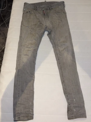 Grå slim / skinny jeans från Dsquared2 - Snygga grå slim/ skinny jeans från Dsquared2 med slitna detaljer och diskret tvättad look. Jeansen har klassisk femficksdesign och knappgylf med Dsquared2-logga. Perfekta för en trendig och avslappnad stil.