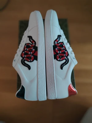 Gucci ace med orm - Snygga vita sneakers från Gucci med broderad röd och svart orm på sidorna. Helt nya o har aldrig använt dom