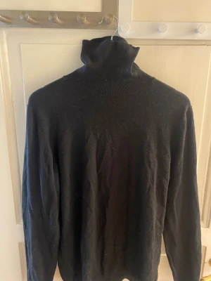 Svart polotröja i stickat material - Klassisk svart stickad polotröja med hög krage och långa ärmar. Tröjan har en enkel och stilren design som passar till det mesta. Perfekt för lager på lager och en snygg bas i garderoben.