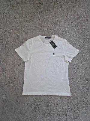 Polo Ralph Lauren - Klassisk vit t-shirt från Polo Ralph Lauren med rund hals och korta ärmar. T-shirten har den ikoniska lilla broderade loggan på bröstet och är tillverkad i mjuk bomull för en skön känsla.