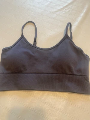 Mörkgrå ribbad body med smala band - Snygg mörkgrå body med smala, justerbara axelband och ribbad nederkant. Enkel och stilren design utan synliga loggor eller mönster. Perfekt att bära under kläder eller som ett basplagg. Materialet känns mjukt och stretchigt.