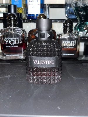 Valentino parfym - Säljer en lyxig parfym från Valentino i en mörk, nitprydd glasflaska med svart etikett och detaljer. Flaskan har en unik, kantig design med struktur och svart lock. Perfekt för dig som gillar exklusiva dofter och snygg design.Ca 40ml kvar
