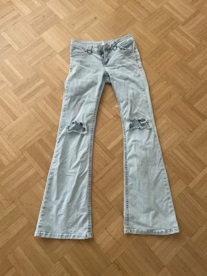 Ljusblå bootcut jeans med hål - Säljer ett par ljusblå bootcut jeans med slitna hål på båda knäna. värt att veta att jeansen blivit missfärgade som man kan se på bild 3 och 4 (inget som verkligen sticker ut) Jeansen har klassisk femficksdesign och vida ben. Perfekta för en avslappnad och trendig look.
