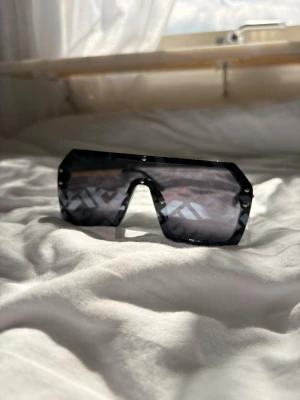 Fendi sol glasögon  - Säljer ett par svarta shield-solglasögon med spegellins och geometrisk form. Glasögonen har en modern, kantig design och bred front som ger en futuristisk vibe. Perfekta för dig som vill sticka ut och addera edge till din look.