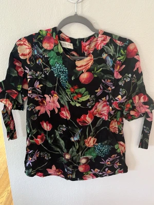 By Malina sidenblus med blommig print - Säljer fin By Malina blus i 100% siden med vacker blommig print (tulpaner, orkidéer och fåglar). Ruffled ärmar med knytband ger en festlig känsla. Jättebra skick! ✨ Perfekt till jeans, kjol eller fest. Lyxig känsla. Frågor? Skriv gärna! Kan skickas snabbt 😊