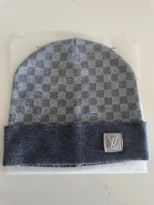Grå mössa med rutmönster - Snygg grå mössa med klassiskt rutmönster. Tillverkad i mjukt och bekvämt material som håller dig varm under kalla dagar. Perfekt accessoar för en trendig streetwear-look.