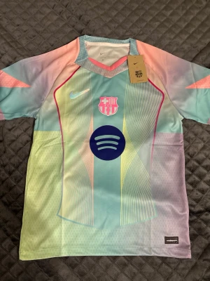 FC Barcelona Nike matchtröja pastell - Säljer en FC Barcelona matchtröja från Nike i snygga pastellfärger med inslag av ljusblått, rosa, gult och lila. Tröjan har klubbmärke, Nike-logga och Spotify som sponsortryck. Tillverkad i lätt och ventilerande Dri-FIT-material, perfekt för träning eller match.