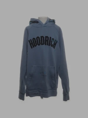 Blå hoodie från Hoodrich - Snygg blå hoodie från Hoodrich med stor svart logga på bröstet och tryck på huvan. Klassisk känguruficka framtill och ribbade muddar vid ärmar och nederkant. Perfekt för en avslappnad streetwear-look. Stolek s man kan va lite mindre