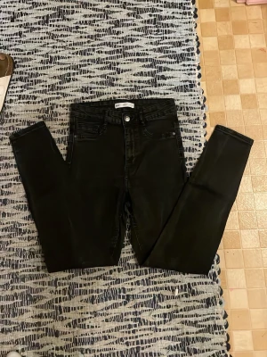 Svarta skinny jeans Gina Tricot - Säljer ett par svarta skinny jeans från Gina Tricot med hög midja och klassisk femficksdesign. Jeansen har stretchigt material och smal passform hela vägen ner. Perfekta till en avslappnad eller trendig look.