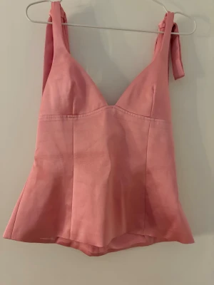 Rosa linnetopp från Zara med knyt - Supersöt rosa linnetopp från Zara med knyt på axlarna och v-ringad hals. Toppen har en lätt utsvängd passform och är tillverkad i ett mjukt material som känns lyxigt mot huden. Perfekt för att lyfta vilken outfit som helst!