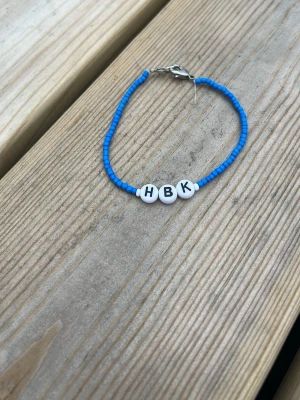 Blått pärlarmband med HBK-bokstäver - Snyggt armband med små blå pärlor och tre vita runda pärlor med bokstäverna H, B och K. Det står för det allsvenska fotbollslaget Halmstad bk. Perfekt för dig som vill supporta ditt lag men på ett lite mindre men meningsfullt sätt. Armbandet har längden 18 cm.