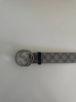 Bälte silverdetalj - Snyggt bälte med klassiskt GG-mönster i grått och svart. Bältet har ett stort, rundat spänne i silverfärgad metall med GG-logga. Perfekt accessoar för att lyfta din outfit.