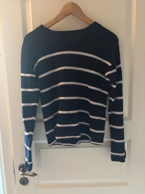 Marinblå randig stickad tröja - Snygg stickad tröja i marinblått med vita horisontella ränder. Tröjan har en klassisk rund halsringning och långa ärmar. Perfekt för dig som gillar en enkel och stilren look. Materialet är mjukt och bekvämt.