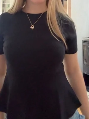 Svart peplum topp - Snygg svart peplum topp med rund hals och korta ärmar. Toppen har en figurnära passform upptill och en utsvängd nederdel som ger en feminin siluett. Perfekt att styla med jeans eller kjol för en trendig look.