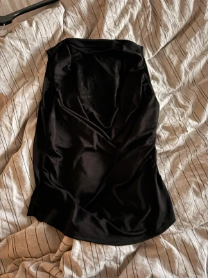 Svart topp med spetsdetaljer - Snygg svart topp med djup V-ringning och spetsdetaljer upptill. Tillverkad i mjukt, stretchigt material som sitter skönt mot kroppen. Spetsen ger en elegant touch och gör bodyn extra fin. Perfekt att styla under en kavaj eller till jeans.