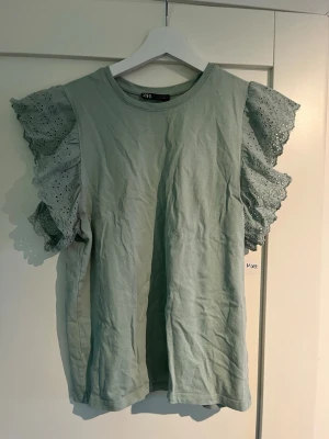Grön topp med volangärmar från Zara - Superfin ljusgrön topp från Zara med broderade volangärmar i bomull. Ärmarna har snygga håldetaljer och ger en cool och unik look. Perfekt att styla med jeans eller kjol för en trendig outfit.