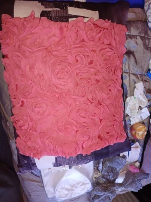 Rosa kuddfodral med rosdetaljer - Säljer ett fyrkantigt kuddfodral i starkt rosa tyg med 3D-blommor i form av rosor på framsidan. Baksidan är slät och enfärgad. Kuddfodralet är gjort i tyg och ger en romantisk och trendig känsla till rummet.