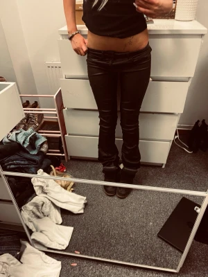 Svarta skinnbyxor med tight passform - Snygga svarta skinnbyxor med tight passform och låg midja. Byxorna har klassisk femficksdesign och utsvängda ben . Perfekta för en edgy och trendig look. Materialet är glansigt och stretchigt. Har tyvärr gått på dem så de är lite slitna vid bakbenen