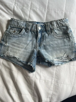 Ljusblå jeansshorts med broderi - Snygga ljusblå jeansshorts med slitna detaljer och råa kanter. Shortsen har klassisk femficksdesign och broderade bakfickor med knappar. Från Gina tricot! 