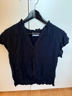 Mörkblå blus från Selected Femme - Säljer en mörkblå blus från med v-ringning och korta ärmar. Blusen har en lätt rynkad krage och är tillverkad i ett tunt, luftigt material som känns skönt mot huden. 