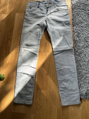Ljusgrå raka chinos - Säljer ett par ljusgrå chinos med rak passform och klassisk femficksdesign. Chinosen har bälteshällor och knappgylf. Materialet ser ut att vara bomullsdenim med en mjuk känsla. Perfekta för en clean och avslappnad stil.