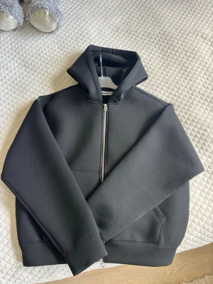 Svart hoodie med dragkedja från Weekday - Säljer en svart hoodie från Weekday i storlek S. Hoodien har dragkedja framtill, stor huva och två fickor. Tillverkad i ett tjockare, mjukt material som känns riktigt skönt. Perfekt för dig som gillar en clean och stilren look.